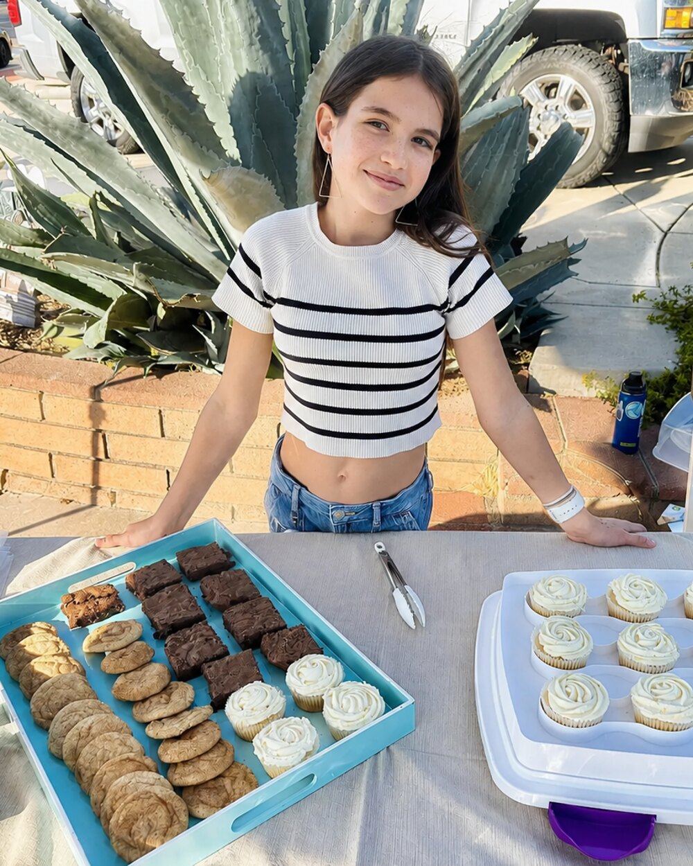 Eliana at her bake-sale stand with trays of cookies and cupcakes